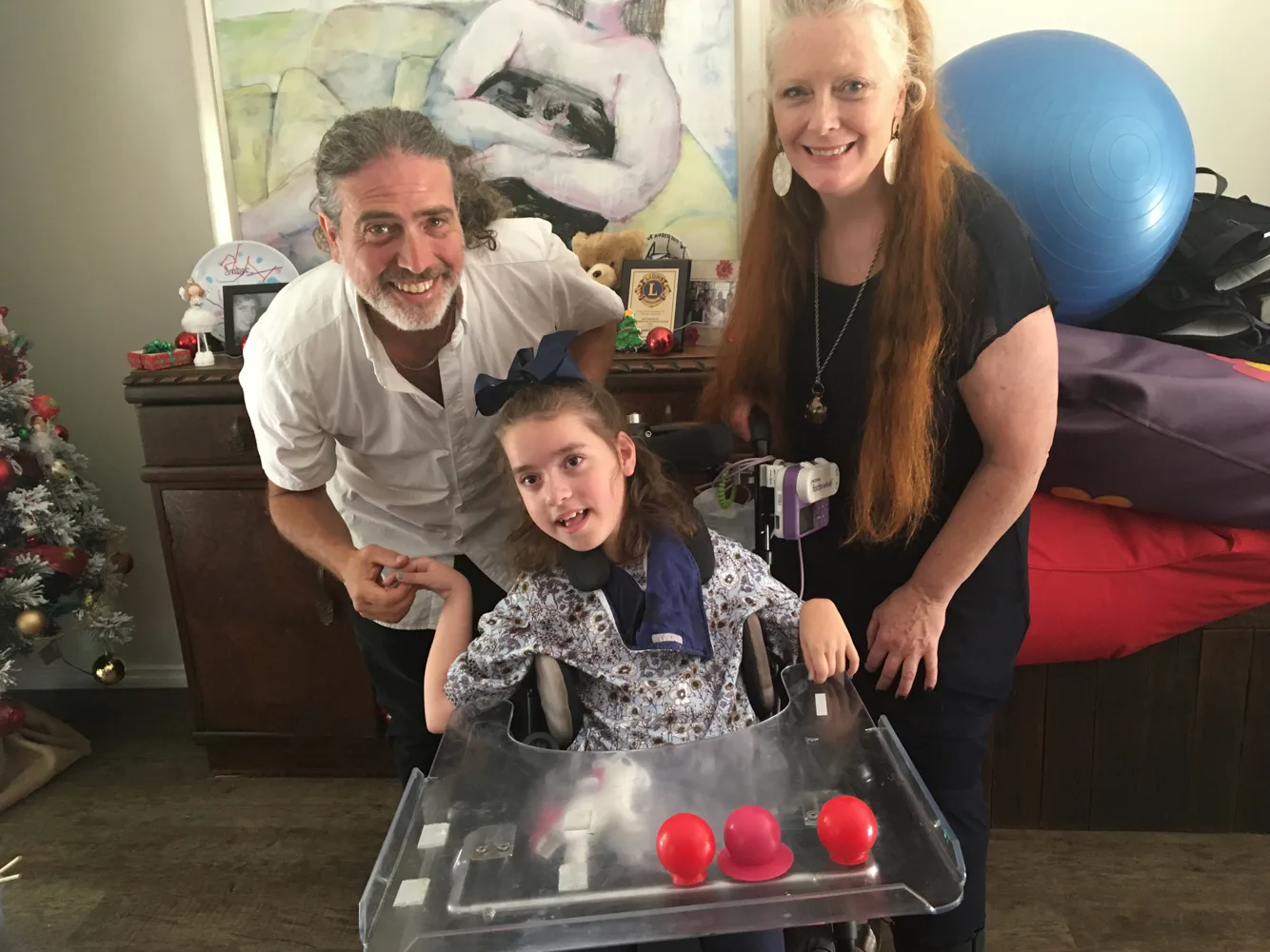 Amber smiles at her play table beside a Safe in Sound musician and her mother